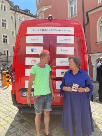 NOAH-Caritas Mobil davor stehend im Gespräch Streetworker Ben Peter mit Vorstandsvorsitzende der Stiftung Johanna Rumschöttel