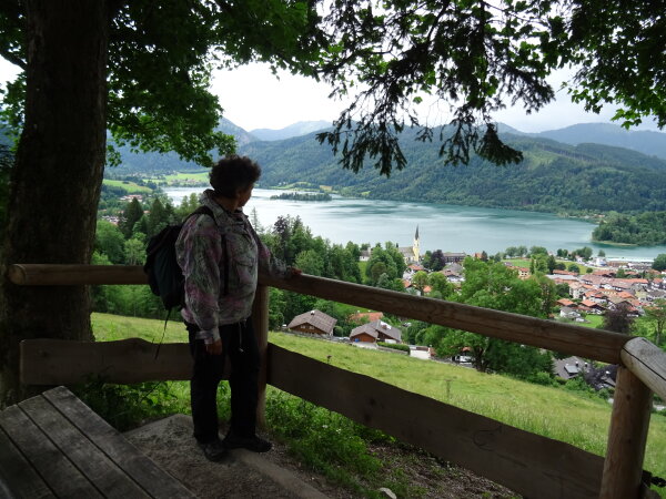 Frau steht neben einen Baum oben auf den Berg und schaut auf den Schliersee