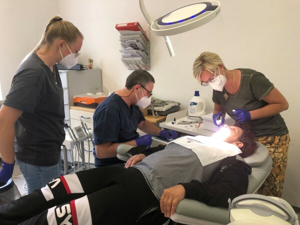 zahnärztliche Behandlung,Patient liegt auf den Zahnarztstuhl und wird von Zahnarzt und Helferin behandelt