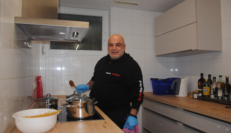Küchenzeile mit Herd, ein Mann kocht Spaghetti auf der anderen Küchenzeile gegenüber stehen Gewürze und Öle