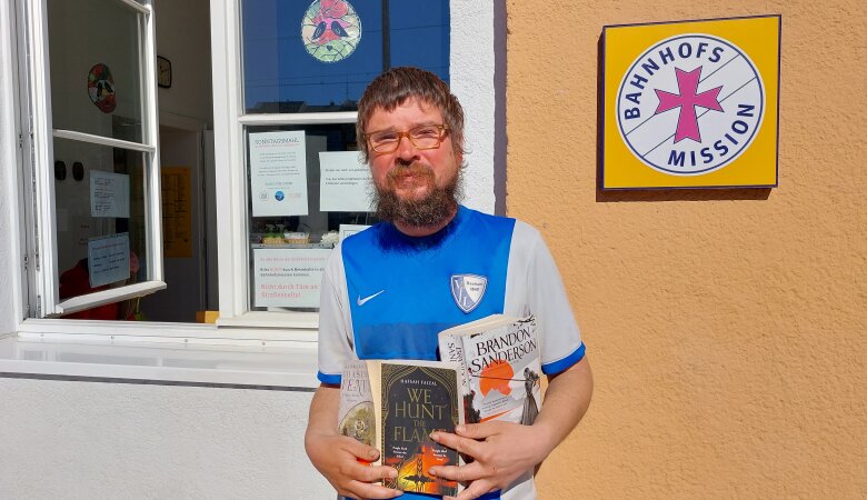 Obdachloser Albert steht vor der Bahnhofsmission und hält Bücher in seinen Händen 
