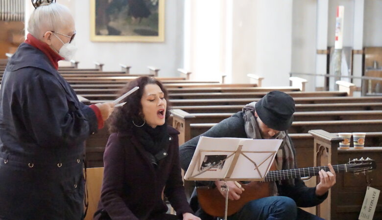 Zwei Musiker sitzen in der Kirche ein Mann spielt Gitarre eine Frau singt eine andere Frau steht danehben